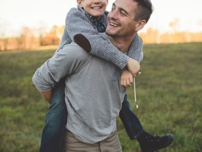 Boy getting piggy back from father in field